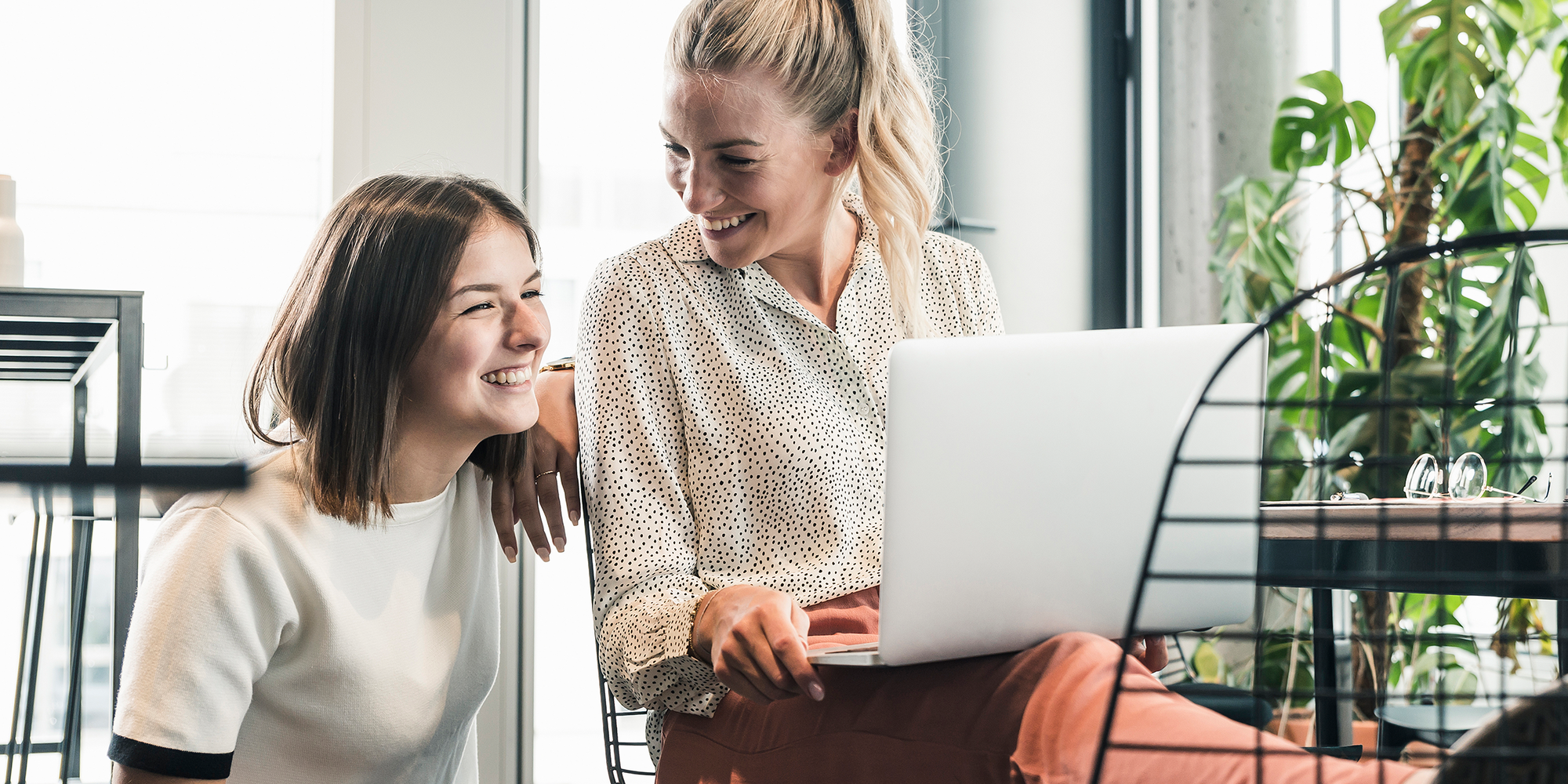 Zwei junge Frauen sitzen lachend an einem Laptop